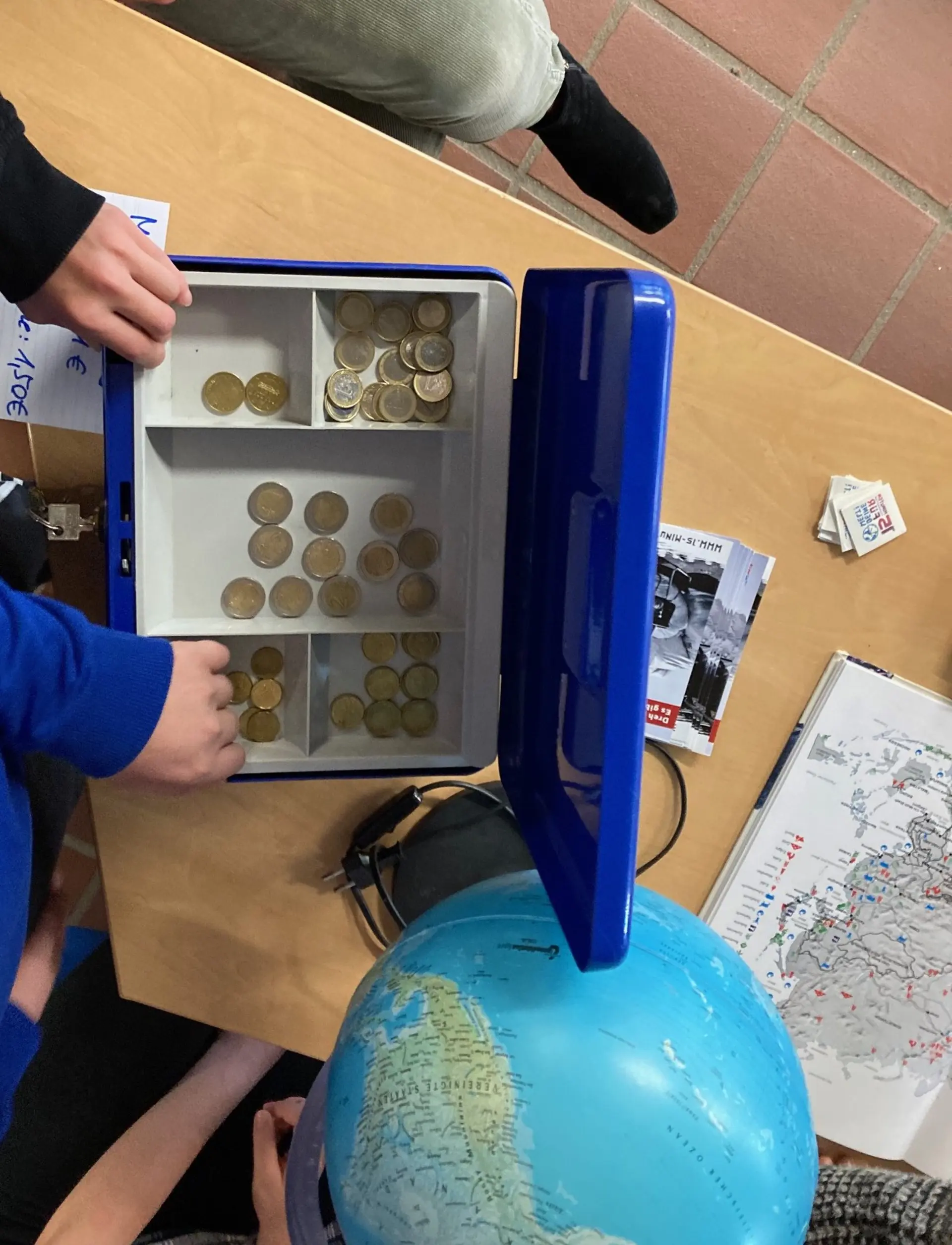 zu sehen ist eine Kasse mit Geld von oben. eine hand legt geld in die kasse.