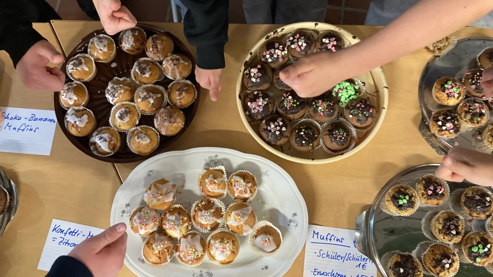 zu sehen sind mehrere Teller mit Muffins von oben. mehrere Hände greifen nach den muffins.