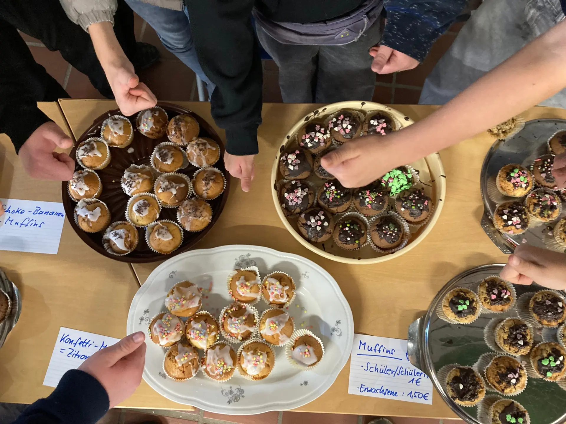 zu sehen sind mehrere Teller mit Muffins von oben. mehrere Hände greifen nach den muffins.