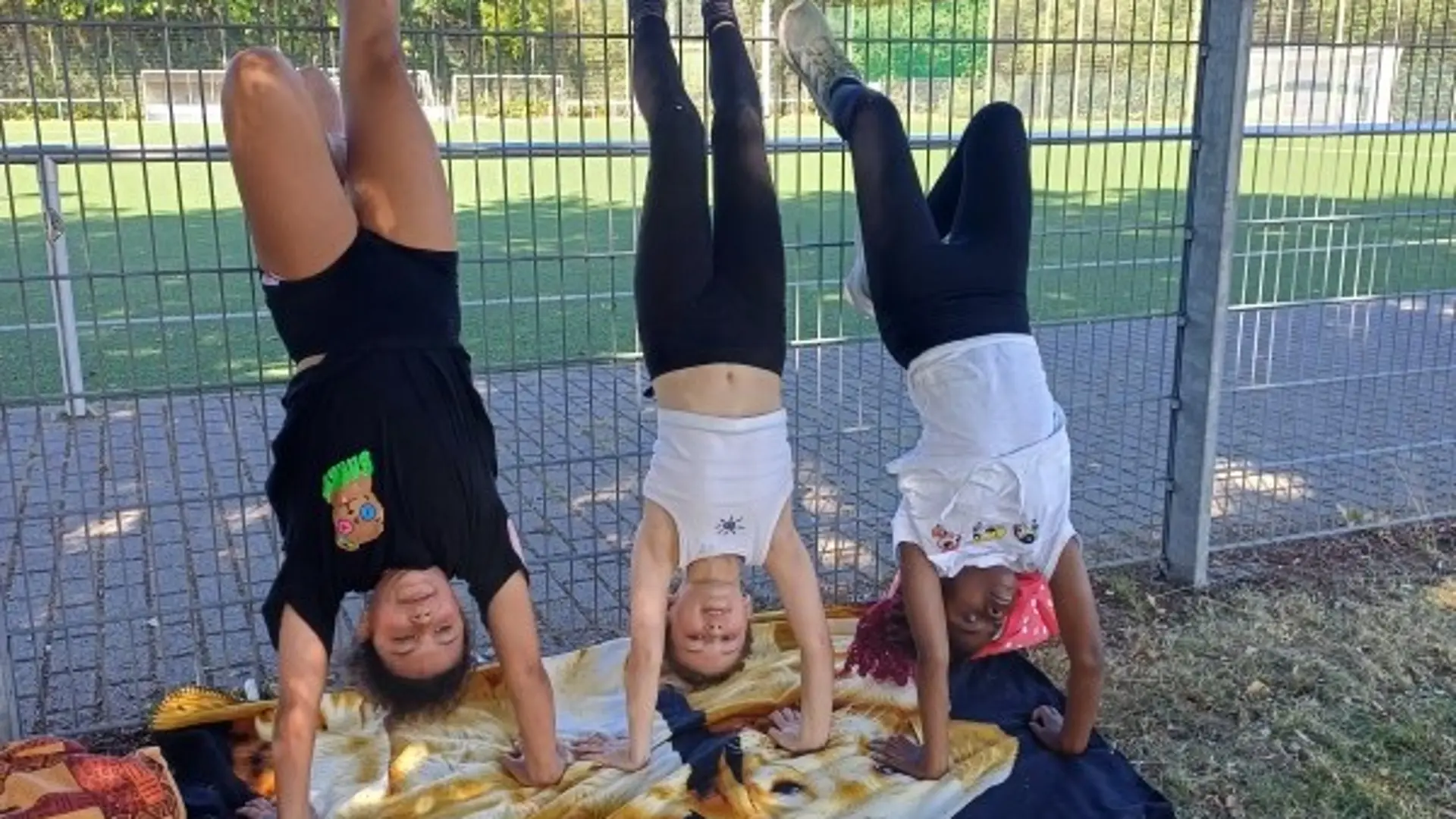 Drei Mädchen machen Handstand an einem hohem Metallzaun