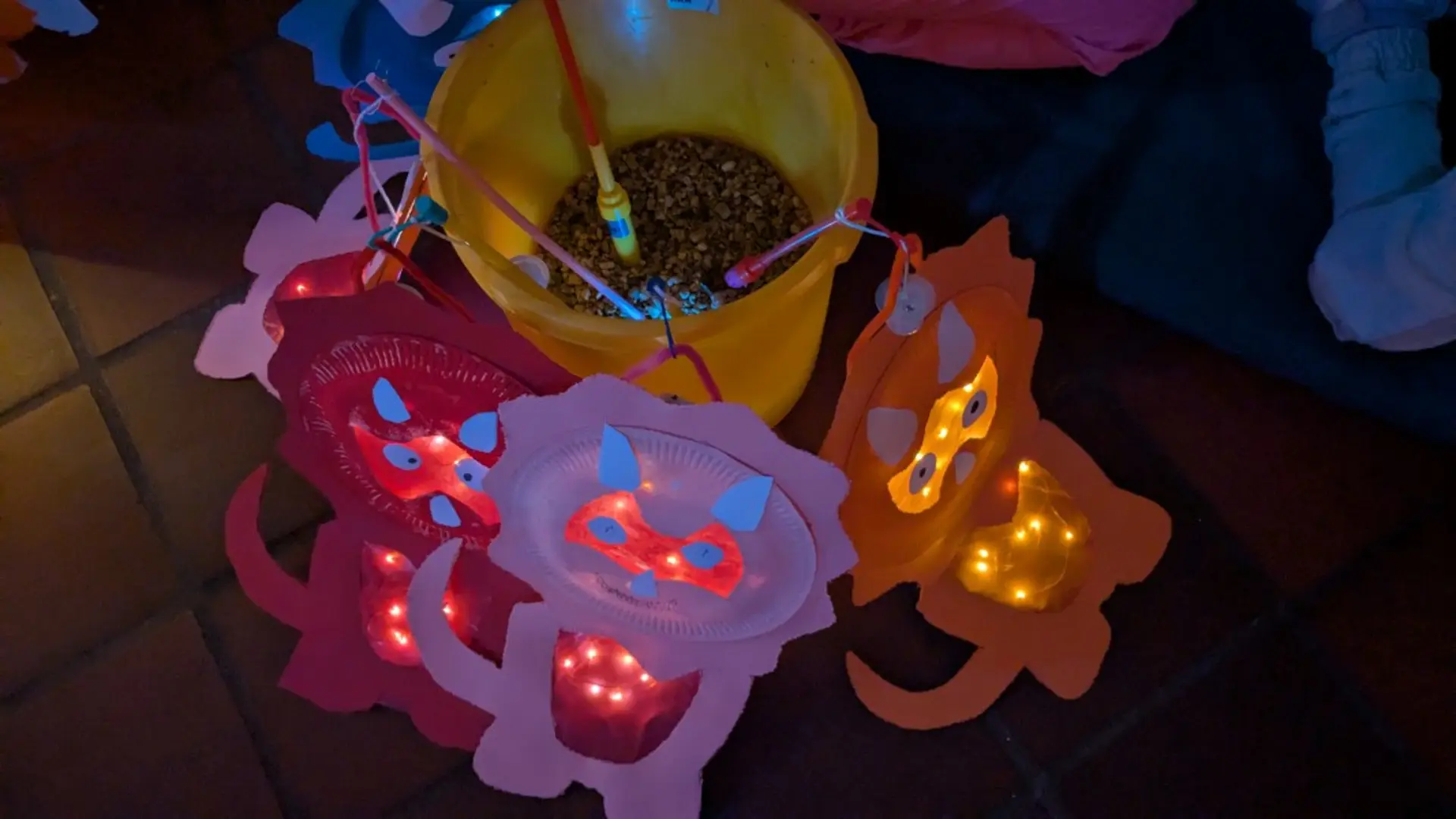 Ein gelber Eimer ist mit Granulat gefüllt. Darin stecken mehrere selbst gebastelte Dinosaurier-Laternen, die im Dunklen leuchten.