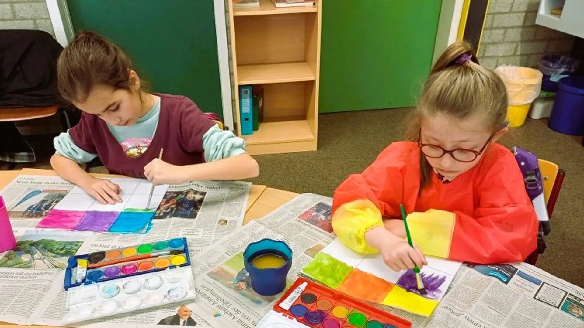 Zwei Grundschülerinnen malen konzentriert mit Wasserfarben.