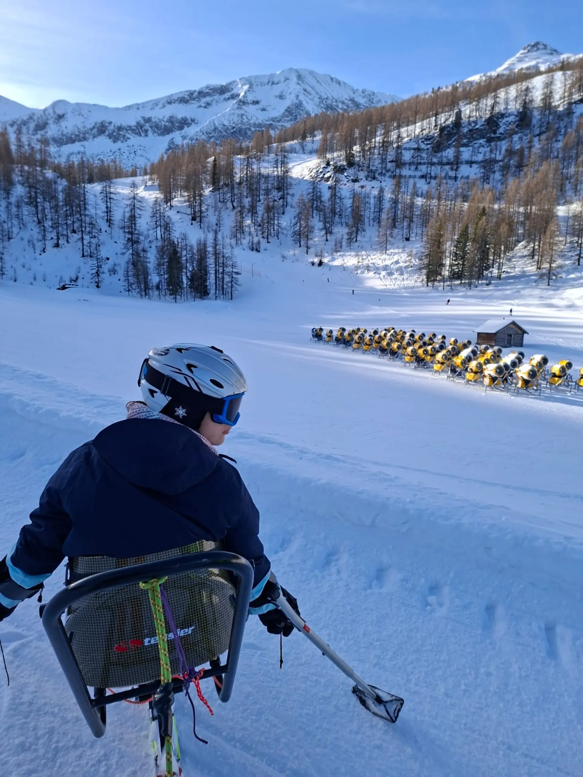 Eine Schülerin sitzt in einer Vorrichtung, die das Skifahren für Rollstuhlfahrer ermöglicht. Sie schaut in die Landschaft.